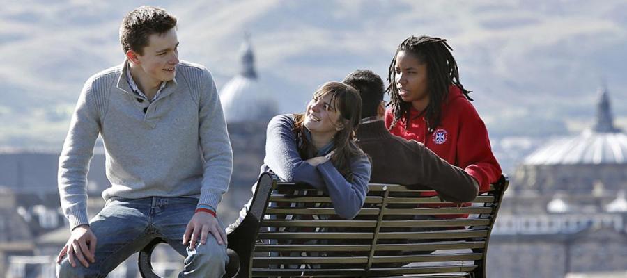 University of Edinburgh students sit on a bench with Edinburgh skyline behind them