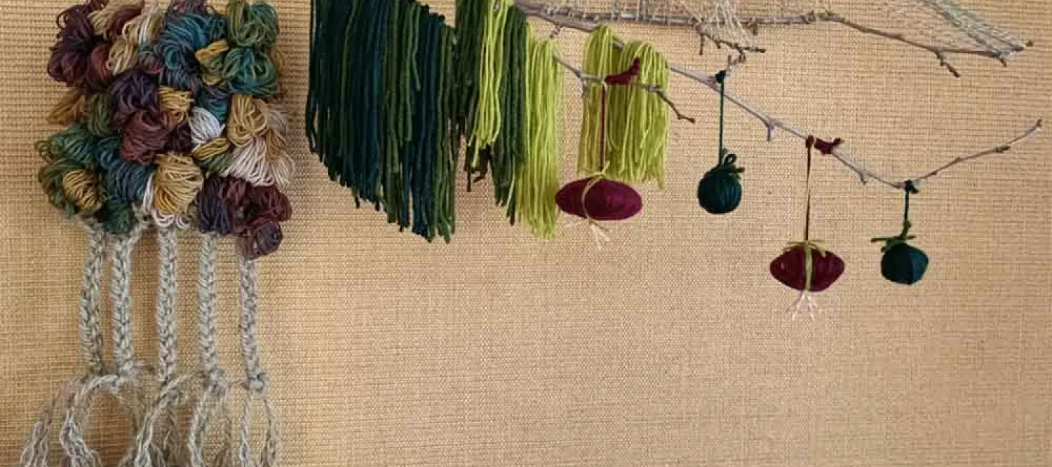 A mixed-medium artwork, made from a branch with wool and string wrapped around it.