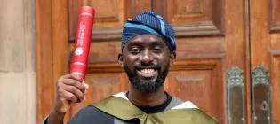 Hammed Kayode Alabi smiling at the camera holding a red University of Edinburgh-branded award.