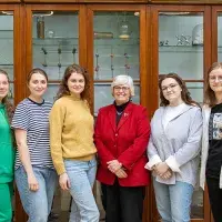 Six people standing and smiling in front of a cabinet filled with scientific devices.