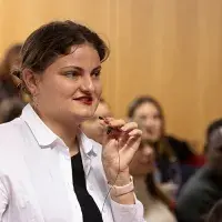 A young person holding a small microphone speaking to a group.