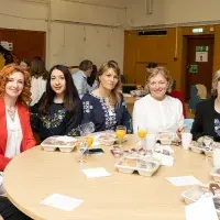 Seven people sitting at a table with food and drinks in the University of Edinburgh's Chaplaincy. Some people wear traditional Ukranian blouses.