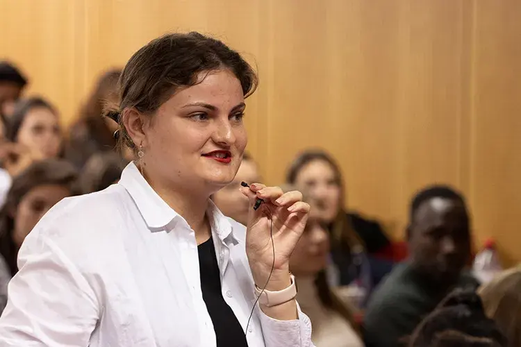 A young person holding a small microphone speaking to a group.