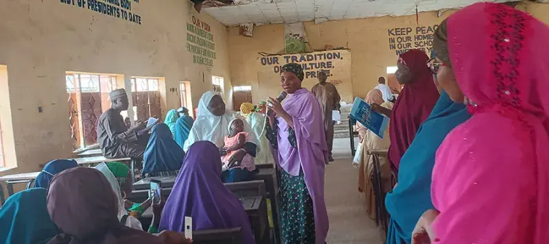 A group of people in Nigeria listening to a person speak with a microphone.
