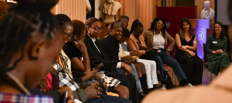 A group of Mastercard Foundation Scholars and staff sitting and talking at an event.