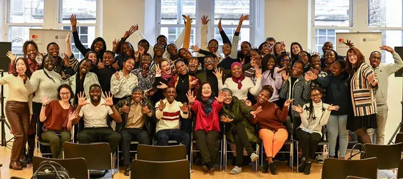 A group of Mastercard Foundation Scholars sitting and standing in a classroom smiling at the camera.