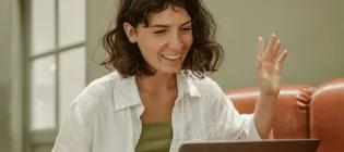 A person speaking and waving to someone on their laptop.