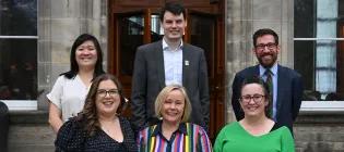 Six people smiling at the camera in front of a University of Edinburgh building.